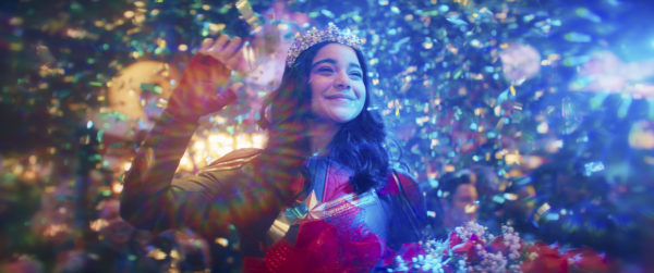 A teen girl in a red and blue superhero costume with a crown, surrounded by confetti