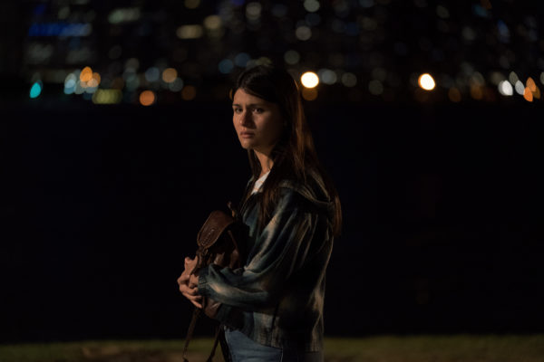 A woman looking scared standing in front of a dark park