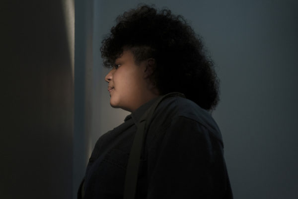 A woman peers through a door as the light shines on her face