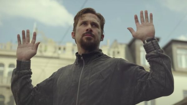 A blonde haired man with moustache raises his arms in a public square