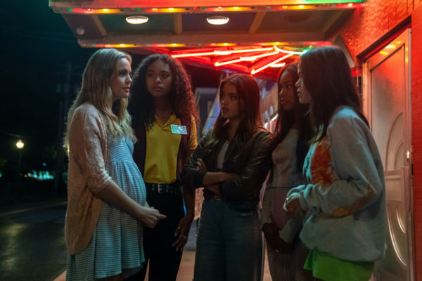 Five girls stand in the street under a neon sign