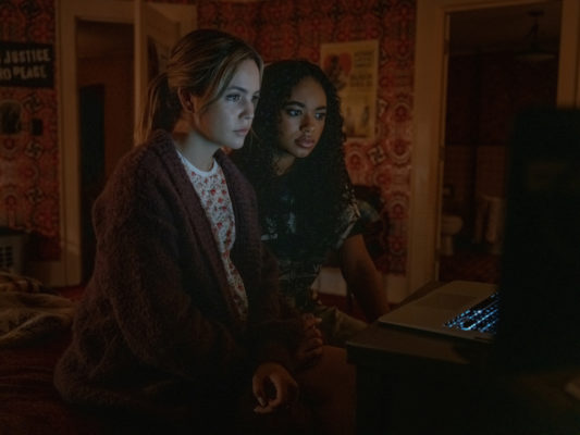 A two girls sit in the dark looking at a computer