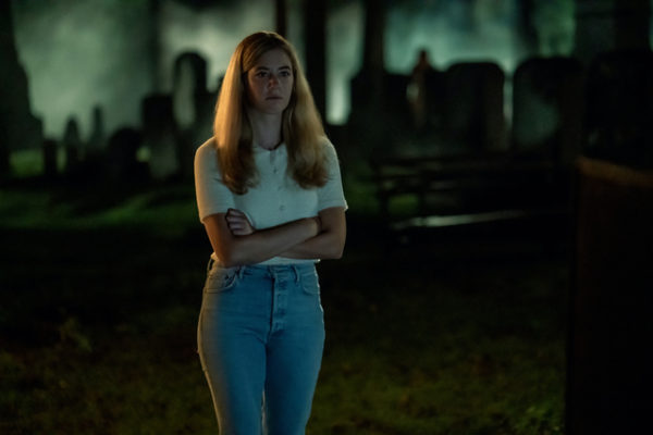 A girl stands in a dark cemetery with her arms crossed