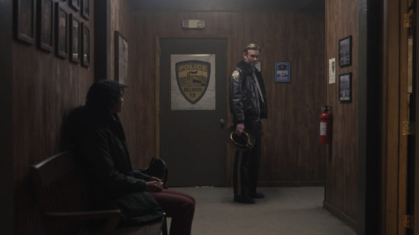 A woman sits in a hallway (L) as the Sheriff (R) looks at her