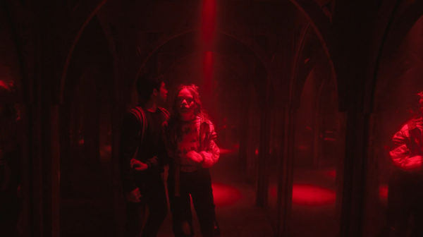 A boy and girl clutch each other in a hall of mirrors in red light