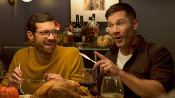 Billy Eichner (L) looks at Luke Macfarlane (R, holding a knife) at a dinner table
