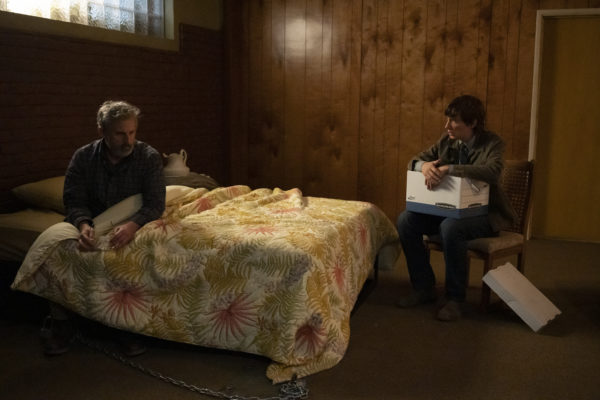 A man (Steve Carell) sits in a bed as a man (Domhnall Gleeson) sits watching him, holding a box