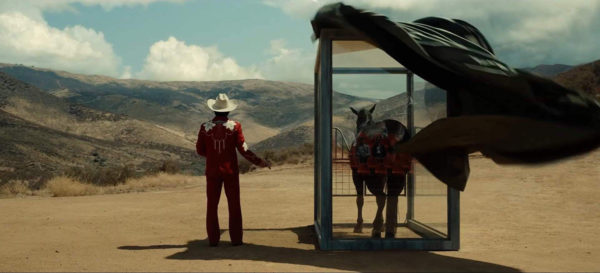 A man (Steven Yuen) standing next to a horse in a glass cage in the desert