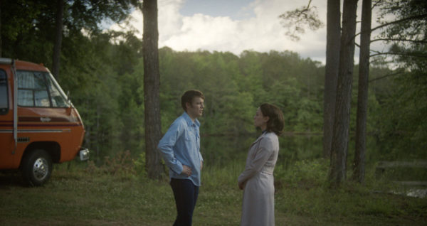 A man (Jake Lacy, L) and woman (Anna Paquin, R) stand in front of a lake in the woods