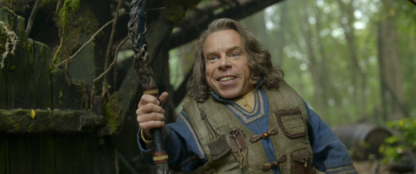 Warwick Davis as Willow, holding a walking stick in the forest