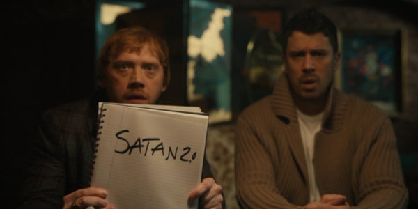Julian (Rupert Grint - R) holding a piece of paper that reads "Satan 2.0" next to Sean (Toby Kebbell - R)