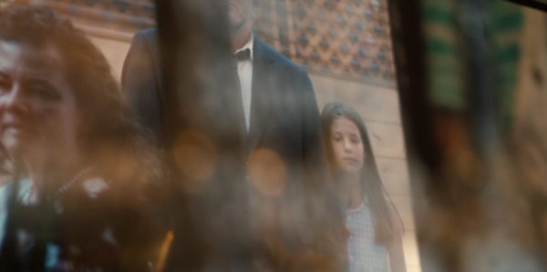 A TV still of a little girl standing next to a man in a tuxedo