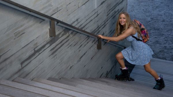 A blonde woman tries to climb the stairs in rollerblades