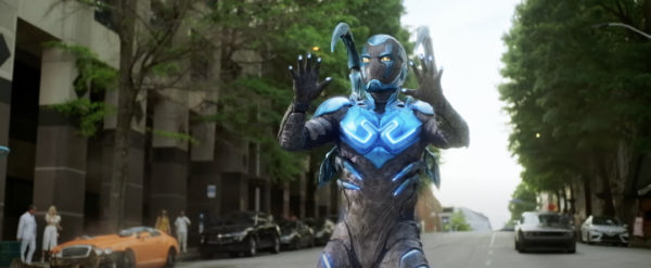 Blue Beetle holds his hands up as he stands in the street