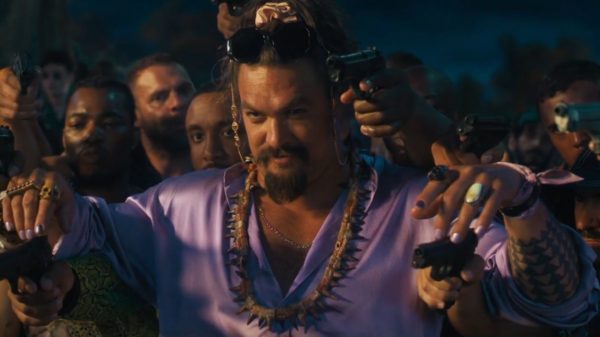 Jason Momoa in a silk purple shirt holding guns