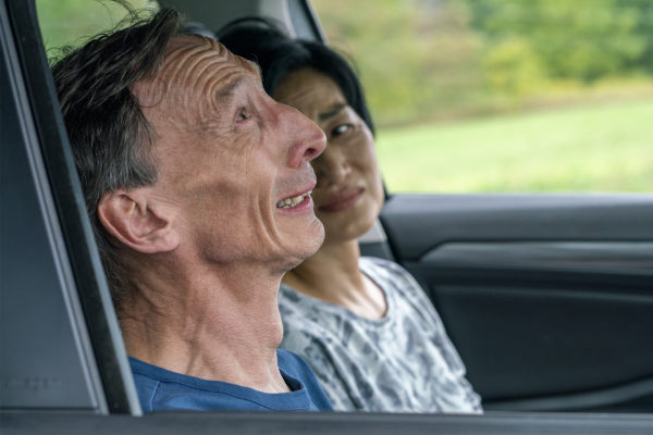 Julian Richings (L - in foreground) and Jean Yoon (R - in background) sit in a car