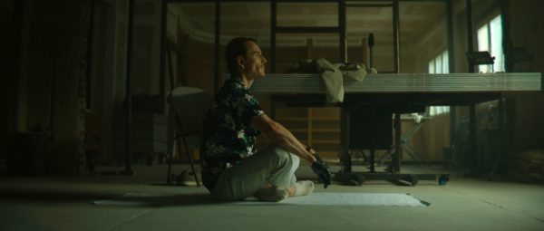 Michael Fassbender as The Killer, sitting cross-legged wearing a tropical button-up, facing right