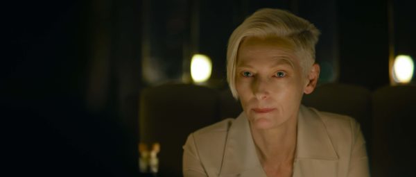 Tilda Swinton as The Expert, leaning forward