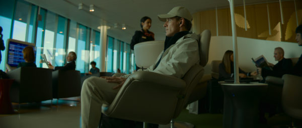 Michael Fassbender as The Killer, sitting in white leather chair in white jogging pants and a baseball cap