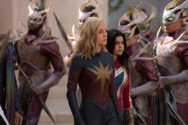Brie Larson as Captain Marvel (L) and Iman Vellani as Ms. Marvel (R) in costume in front of soldiers