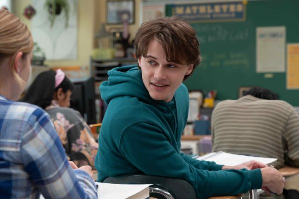 A boy in a green hoodie turns around in his school seat