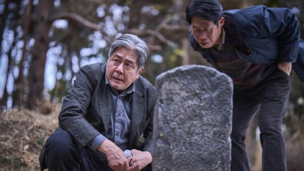 Kim Sang-duk (Choi Min-sik) crouches in front of a tombstone being read by Mr Ko (Yoo Hae-jin)