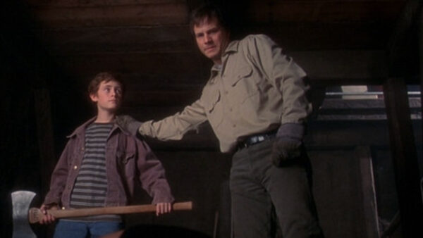 A father (R) places an encouraging hand on the shoulder of his pre-teen son who holds an axe with uncertainty (L)