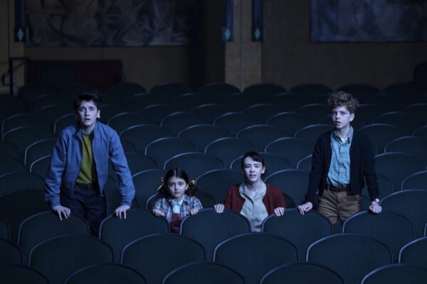 Four pre-teens sit and stand in a dark movie theater