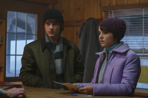 A teenage boy wearing a green winter jacket and black tocque (l) stands next to a pre-teen girl wearing a light purple jacket. She holds a piece of paper