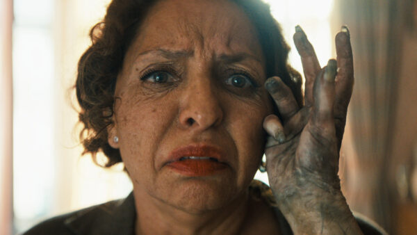 A discoloured hand with long nails strokes the face of a scared looking Hispanic woman