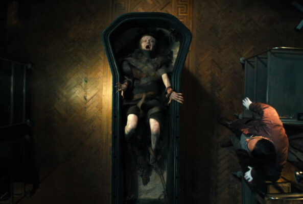 An overhead shot of a girl wrapped in dark bandages, screaming inside a sarcophagus