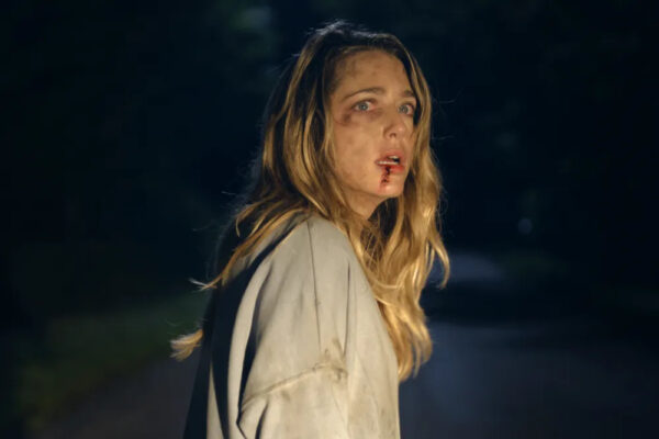 A bloody blonde woman standing in the road in the the headlights of a car