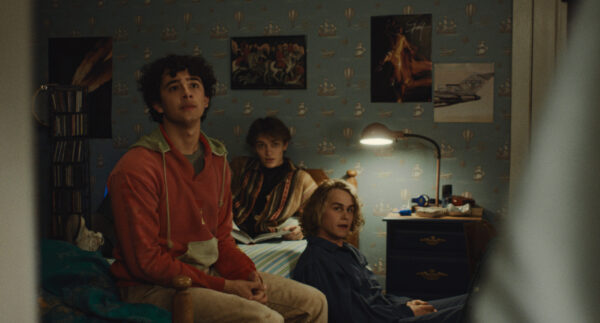 A group of three teenage boys sitting on or around  a bed