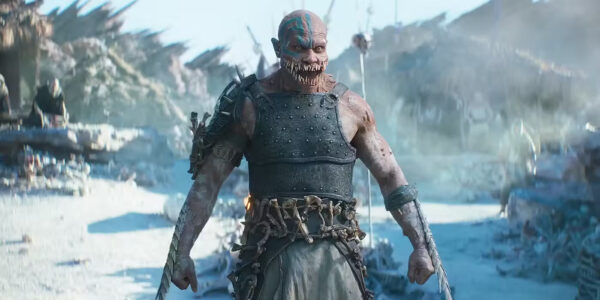 A bald man with an enormous mouth full of jagged teeth, wearing leather body armour