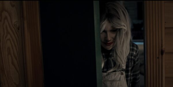 Someone dressed in a Nicole Kidman mask and wig, peering through a half open door