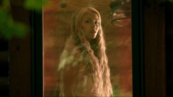 A blonde girl stares through her reflection in a window