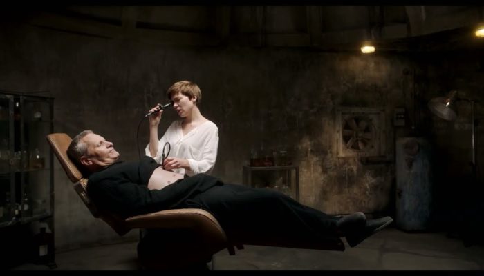 A woman in a white shirt examines a man in black on a reclining chair
