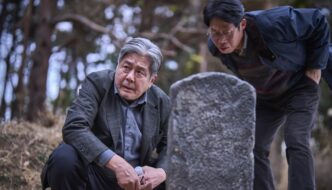 Kim Sang-duk (Choi Min-sik) crouches in front of a tombstone being read by Mr Ko (Yoo Hae-jin)