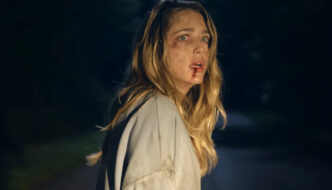 A bloody blonde woman standing in the road in the the headlights of a car