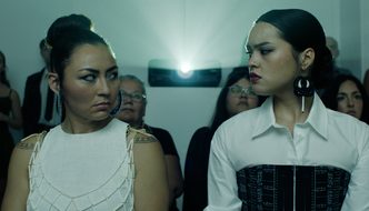 Two Inuit women sit next to each other in a cinema, eyeing each other suspiciously